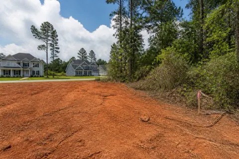 Half-cleared residential lot in a growing Georgia subdivision with graded red clay on one side and pines and survey stakes on the other
